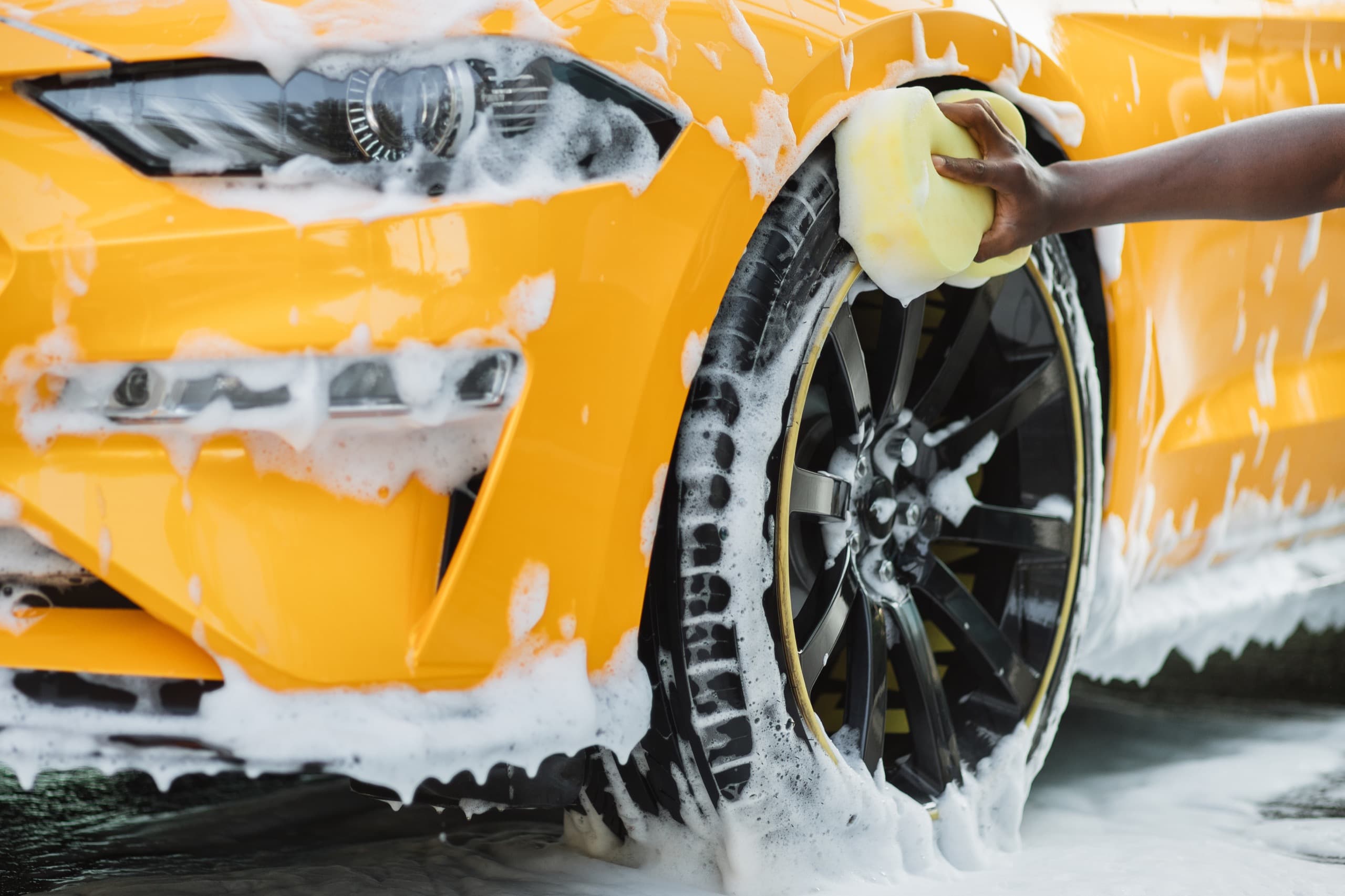 Yellow car wheel being hand washed with foam